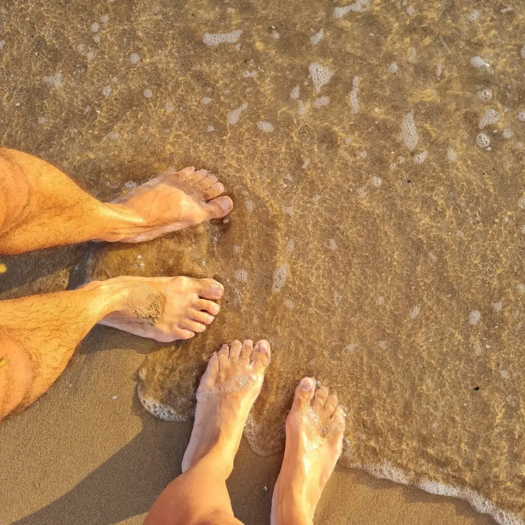 Pies descalzos en contacto directo con la arena y el agua del mar, practicando earthing en la playa